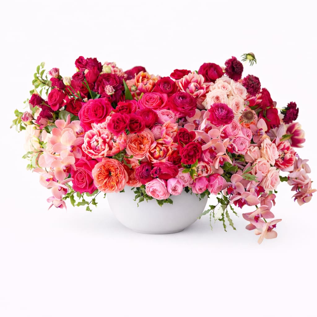 Large pink and red floral arrangement in a white bowl vase