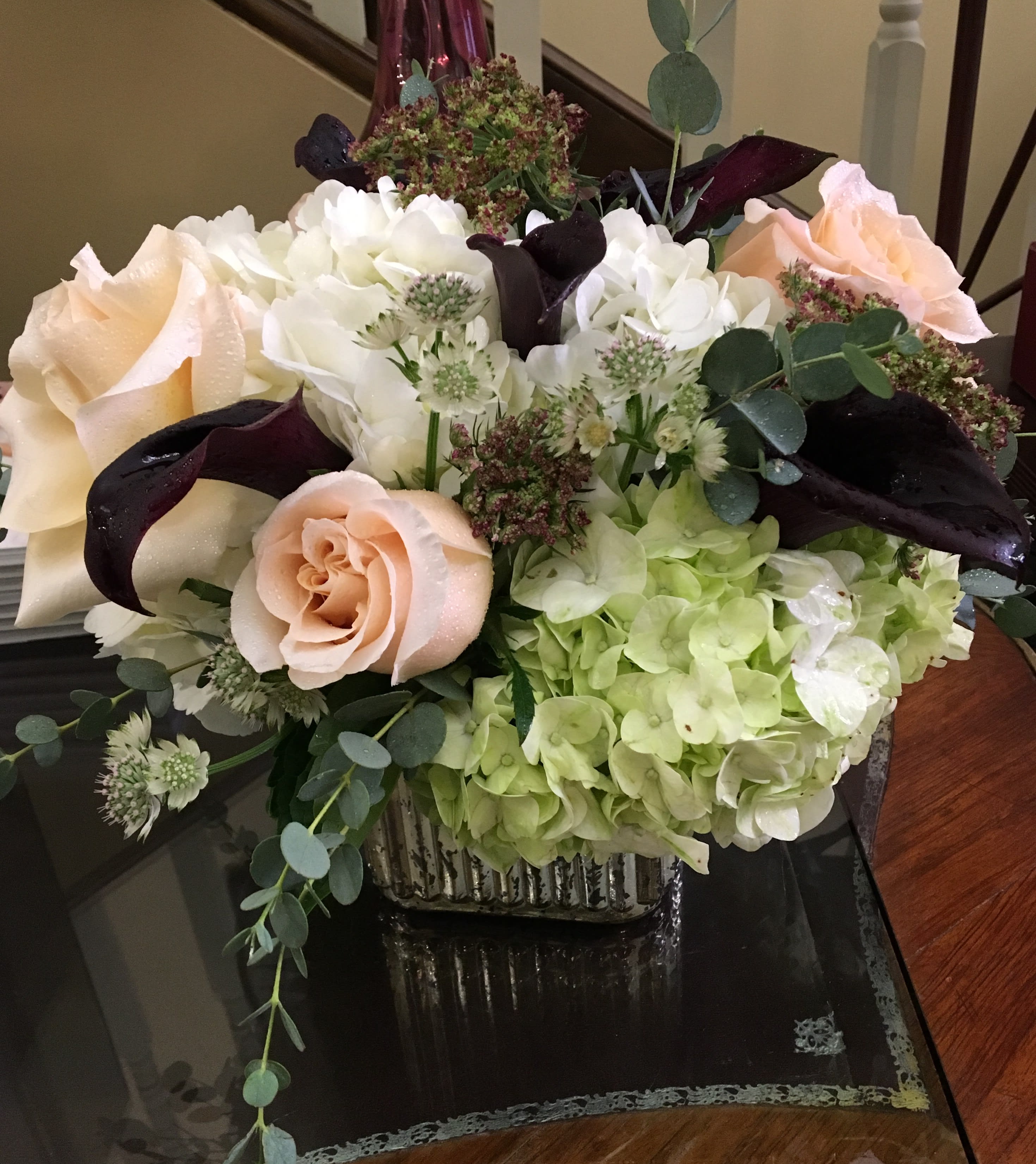 Mixed bouquet with pale roses, white hydrangeas, and dark calla lilies in a square vase