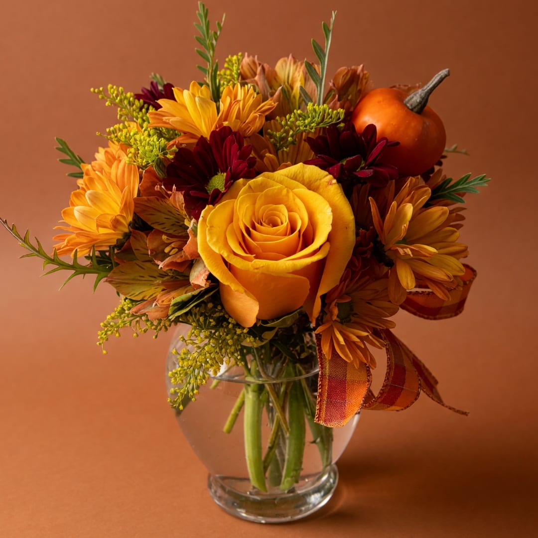 Autumn bouquet of yellow roses and daisies in a clear glass vase with a small pumpkin