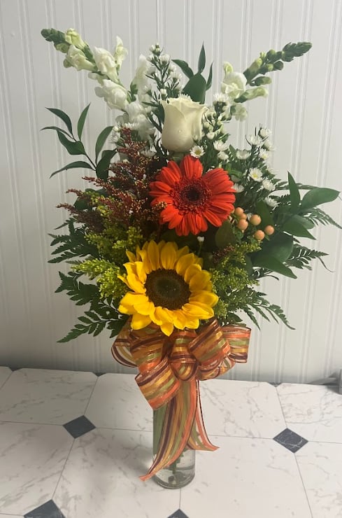 Tall mixed bouquet with sunflowers, a red gerbera daisy, and white blooms in a glass vase