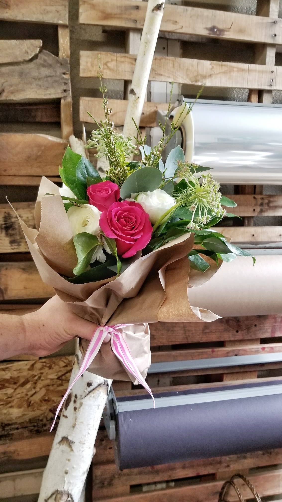 Hand-tied bouquet of pink and white roses wrapped in brown paper
