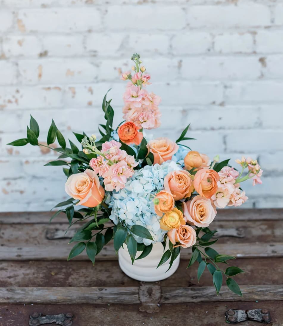 Peach roses and blue hydrangeas in a white vase