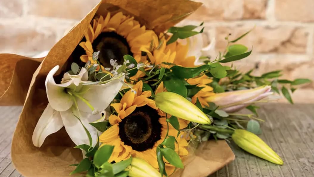 Bouquet with sunflowers, white lilies, and unopened lily buds in brown paper