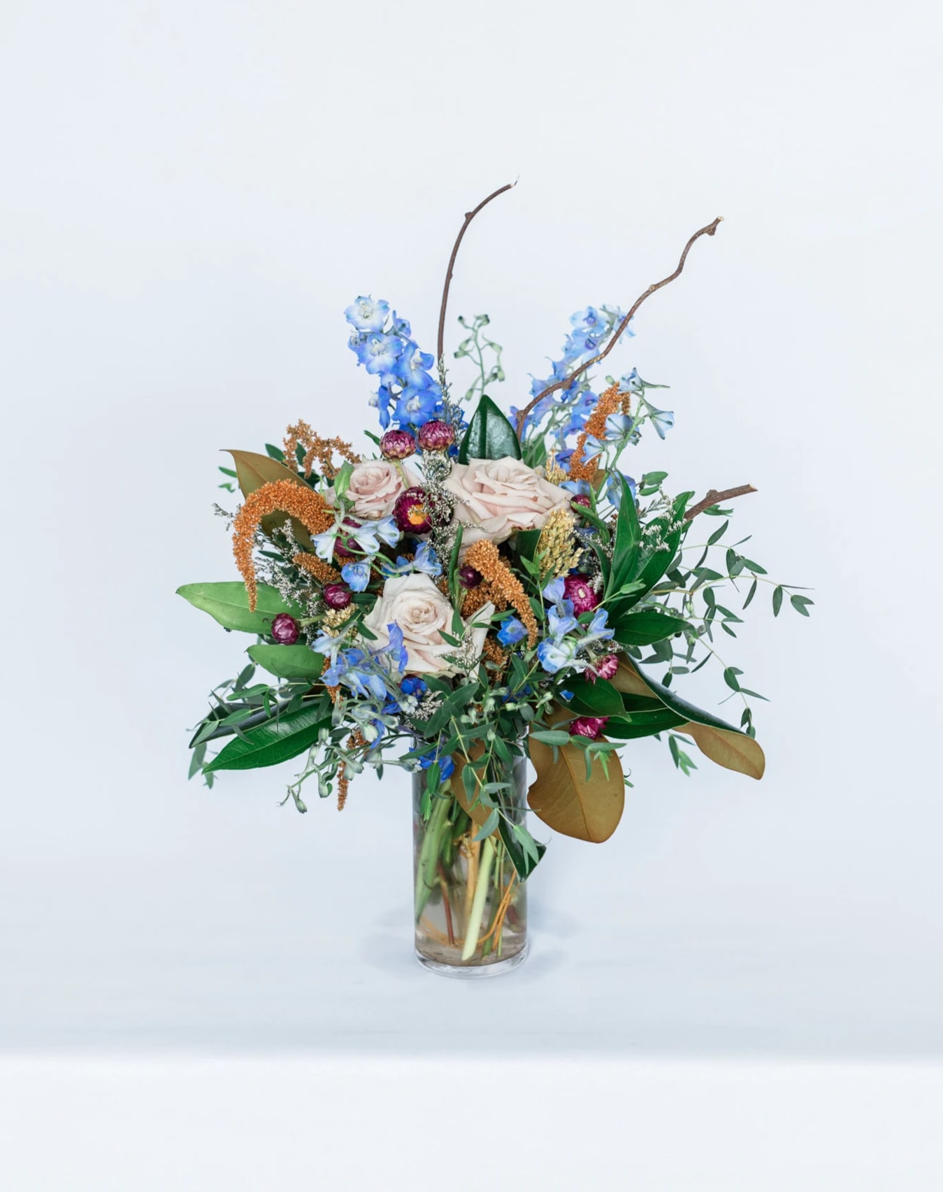 Enchanting Fall - Celebrate the changing of the seasons with our new Fall Collection! Inspired by the autumnal evening skies, the Enchanting Fall comes arranged with a beautiful mix of deep blue, rust, blush, and burgundy premium blooms and textures, all cozily designed in one of our hand-picked designer clear vases.  Pictured [DELUXE]  *Some items in this arrangement must be special ordered, please allow 1-2 weeks notice to allow time for arrival of special items, otherwise, substitutions will occur.*