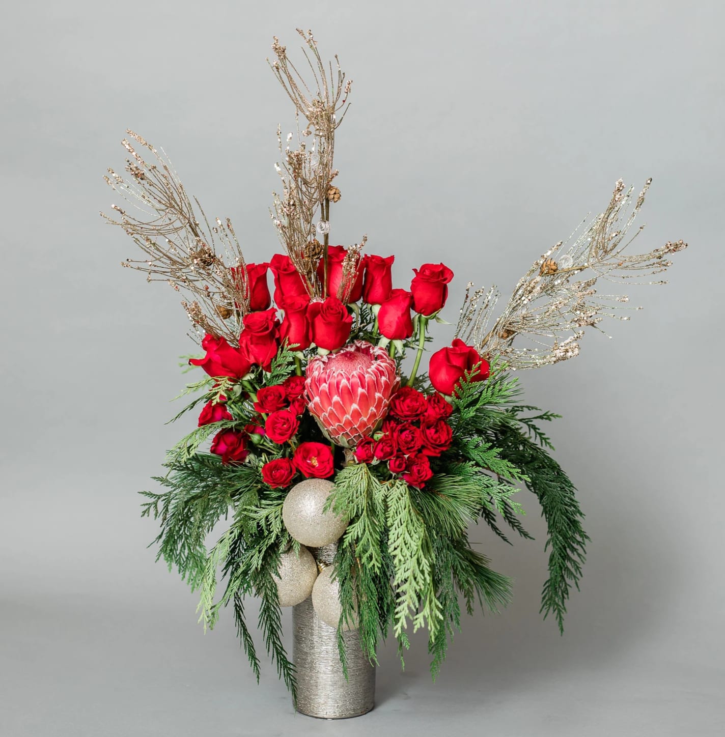 Saint Nicholas' Dream - Get in the Holly Jolly Spirit with our dreamy Holiday Collection! Inspired by the warmth and memories of holidays past, Saint Nicholas' Dream comes arranged with a variety of red premium blooms and textures, accented with holiday greens and glittery decor, all eloquently arranged in one of our hand-picked designer vases.  Pictured [DELUXE]  *Some items in this arrangement must be special ordered, please allow 1-2 weeks notice to allow time for arrival of special items, otherwise, substitutions will occur.*