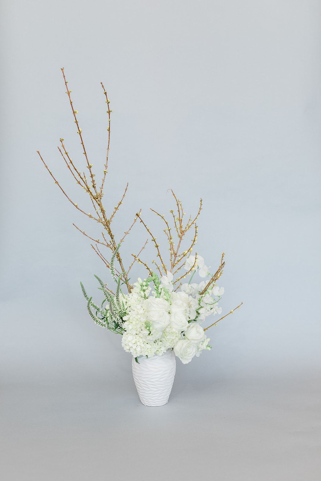 White floral arrangement in a textured white vase with tall branches
