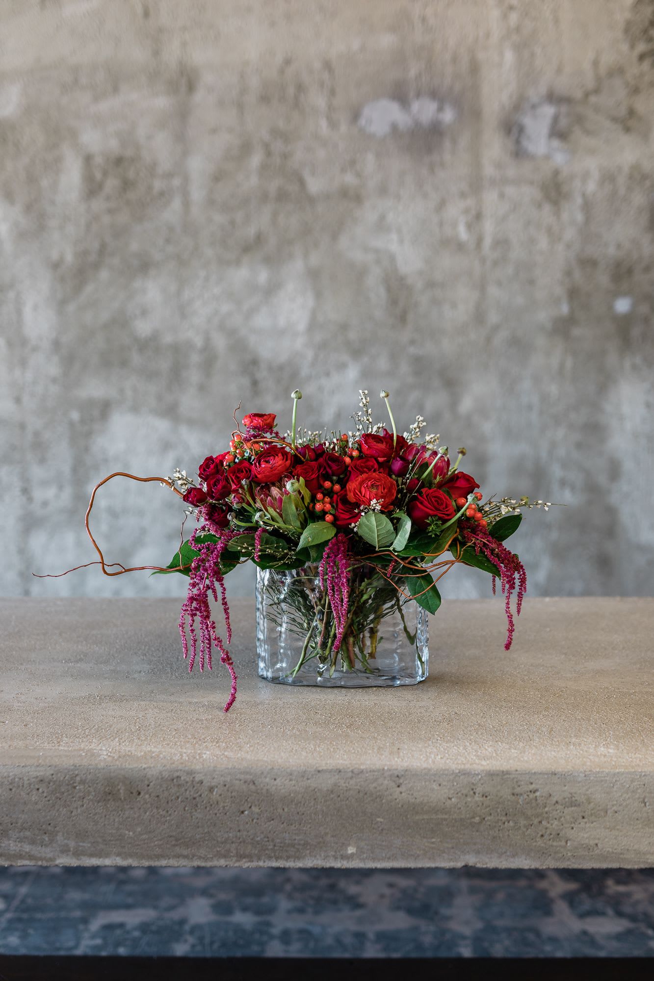 Red rose arrangement in a clear glass vase with trailing pink accents