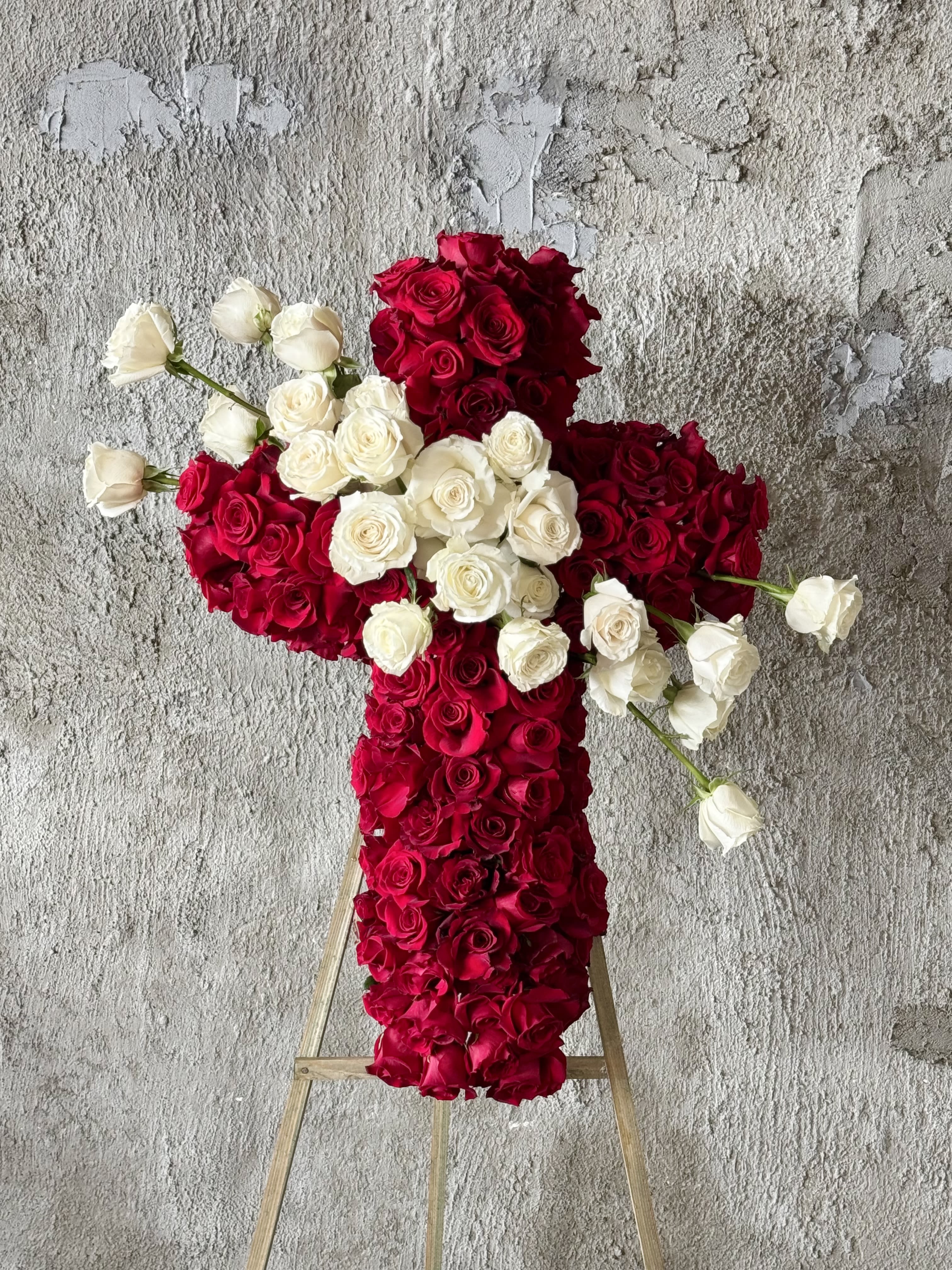 Cross-shaped floral arrangement of red and white roses on a stand