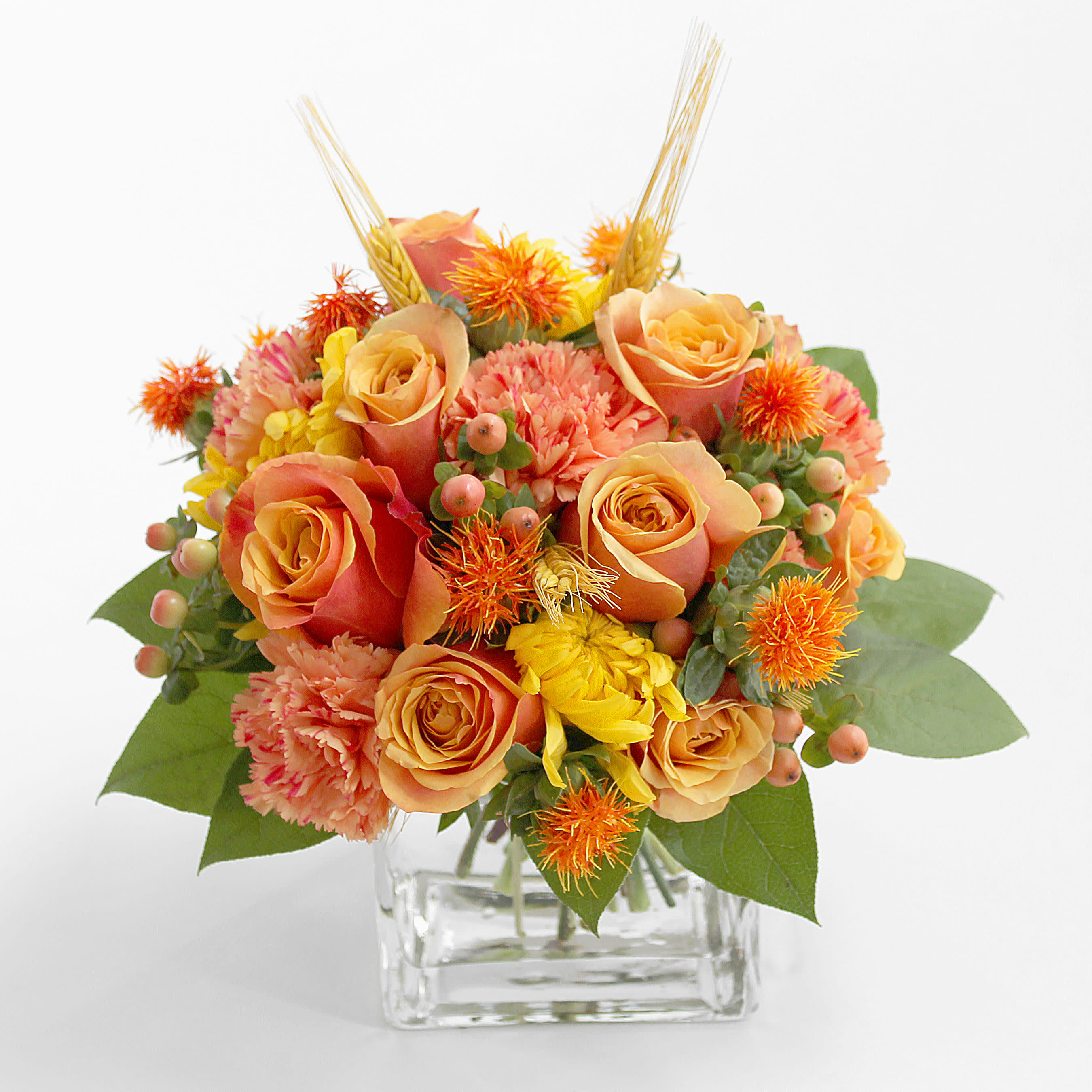 Orange roses and mixed blooms in a clear square vase