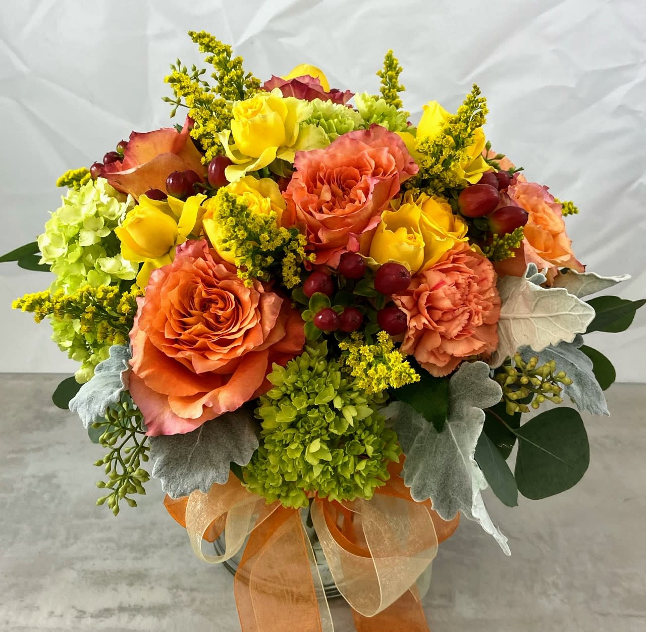 Orange and yellow rose bouquet in a glass vase with ribbon
