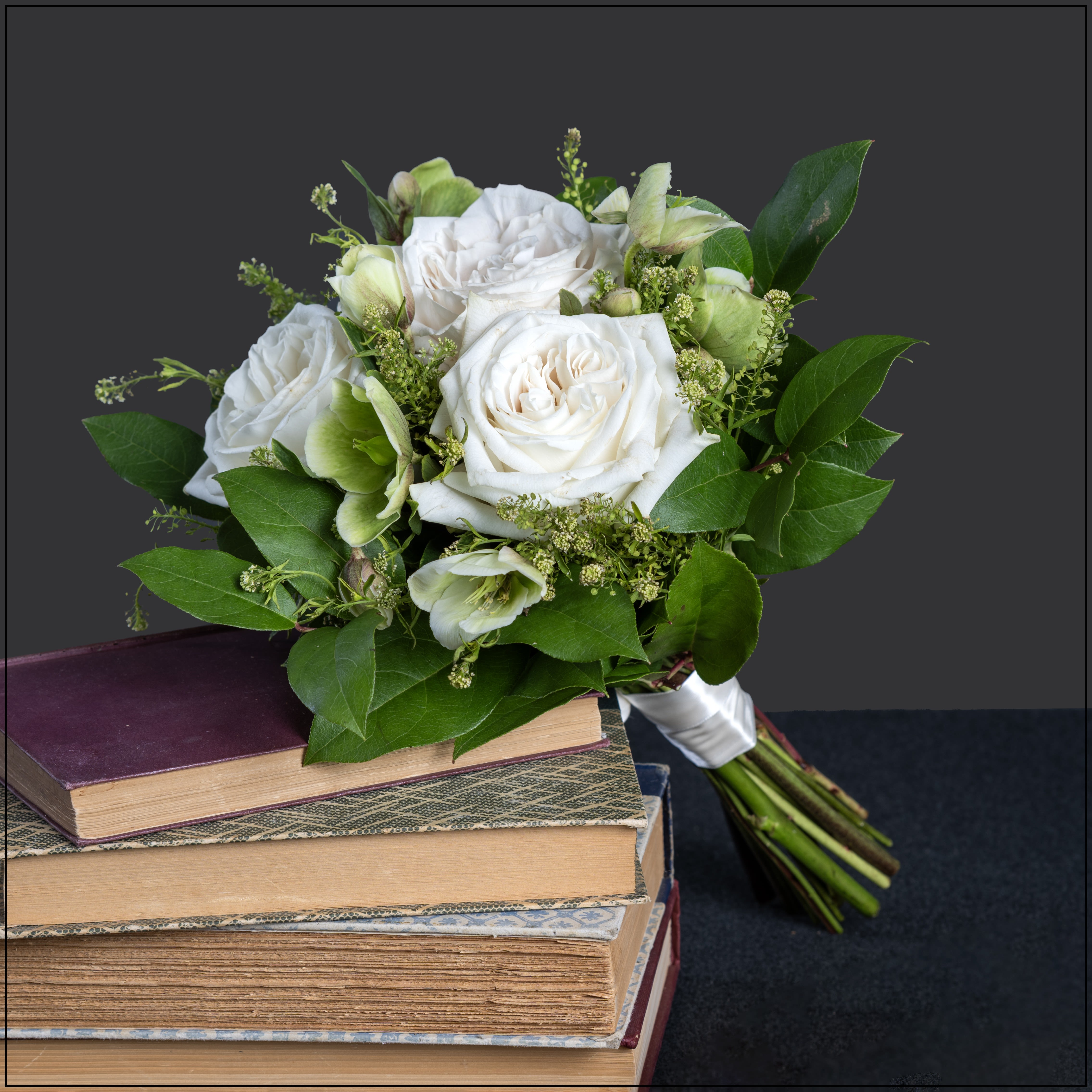 White rose bouquet with green accents resting on stacked books