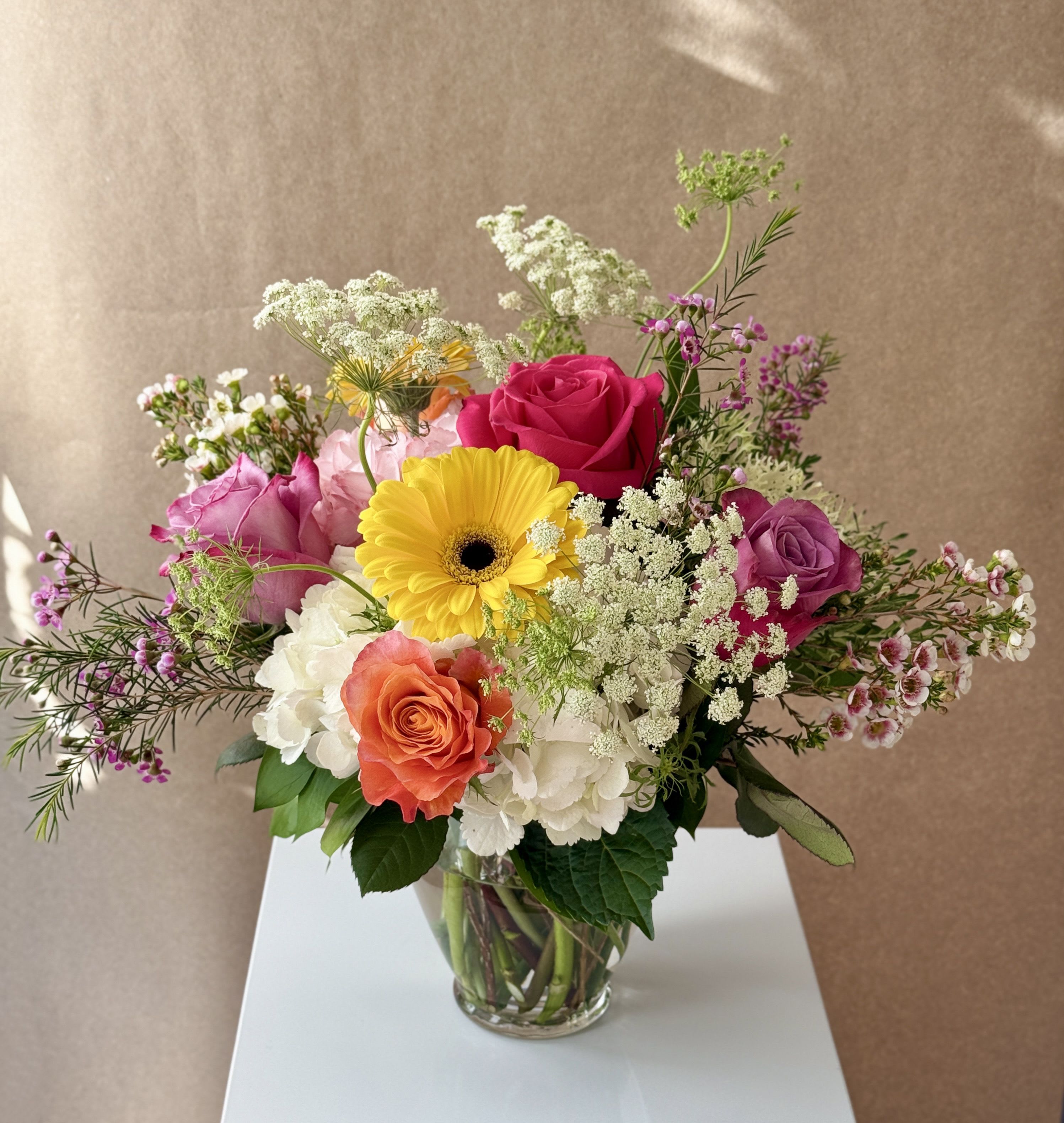 Mixed bouquet of roses, hydrangeas, and a yellow gerbera daisy in a glass vase