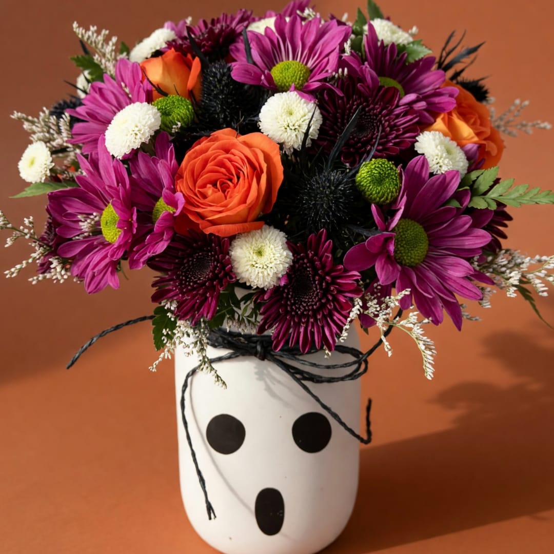 Bouquet of orange roses and purple daisies in a white vase with black dots