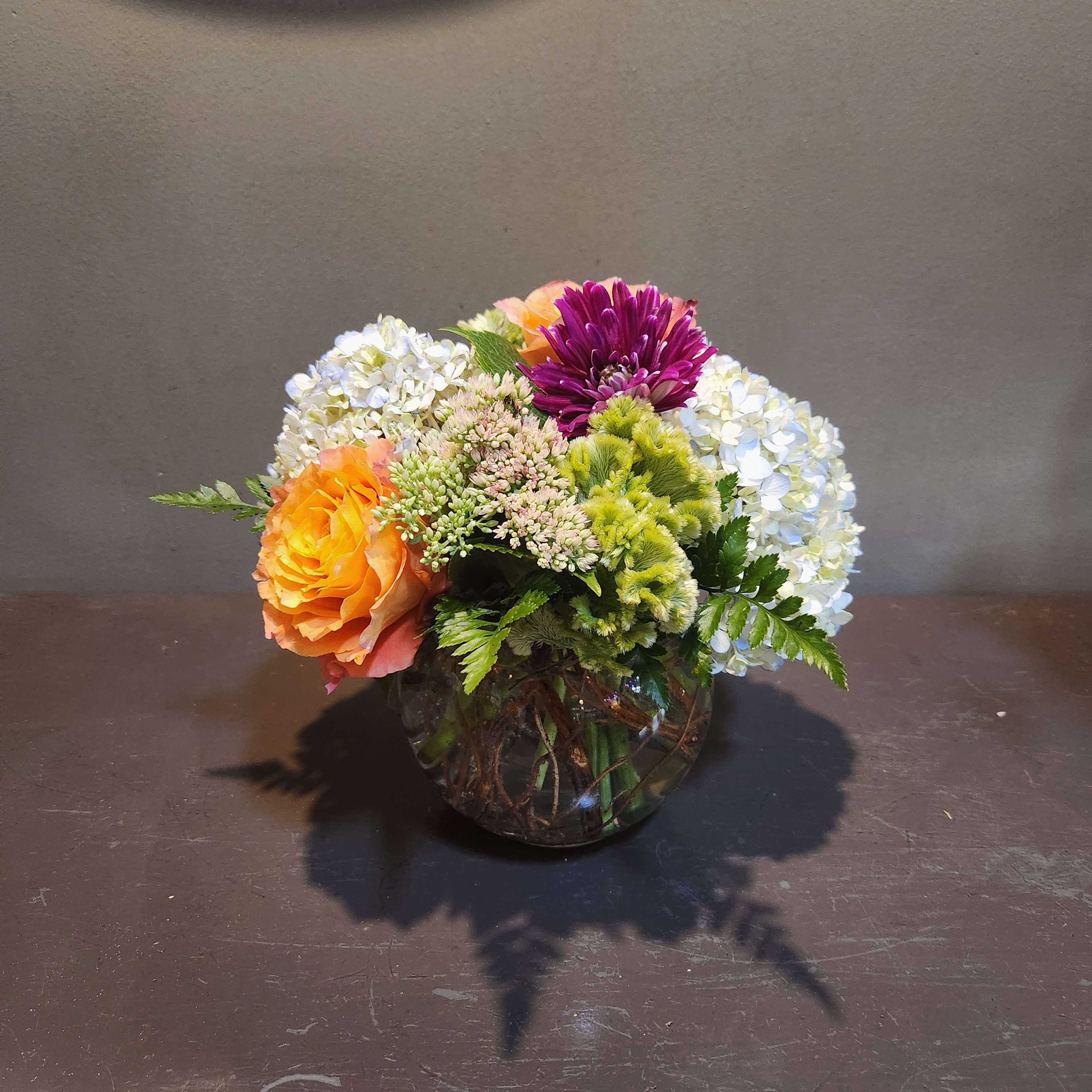 Mixed flower arrangement in a round glass vase with orange, purple, and white blooms