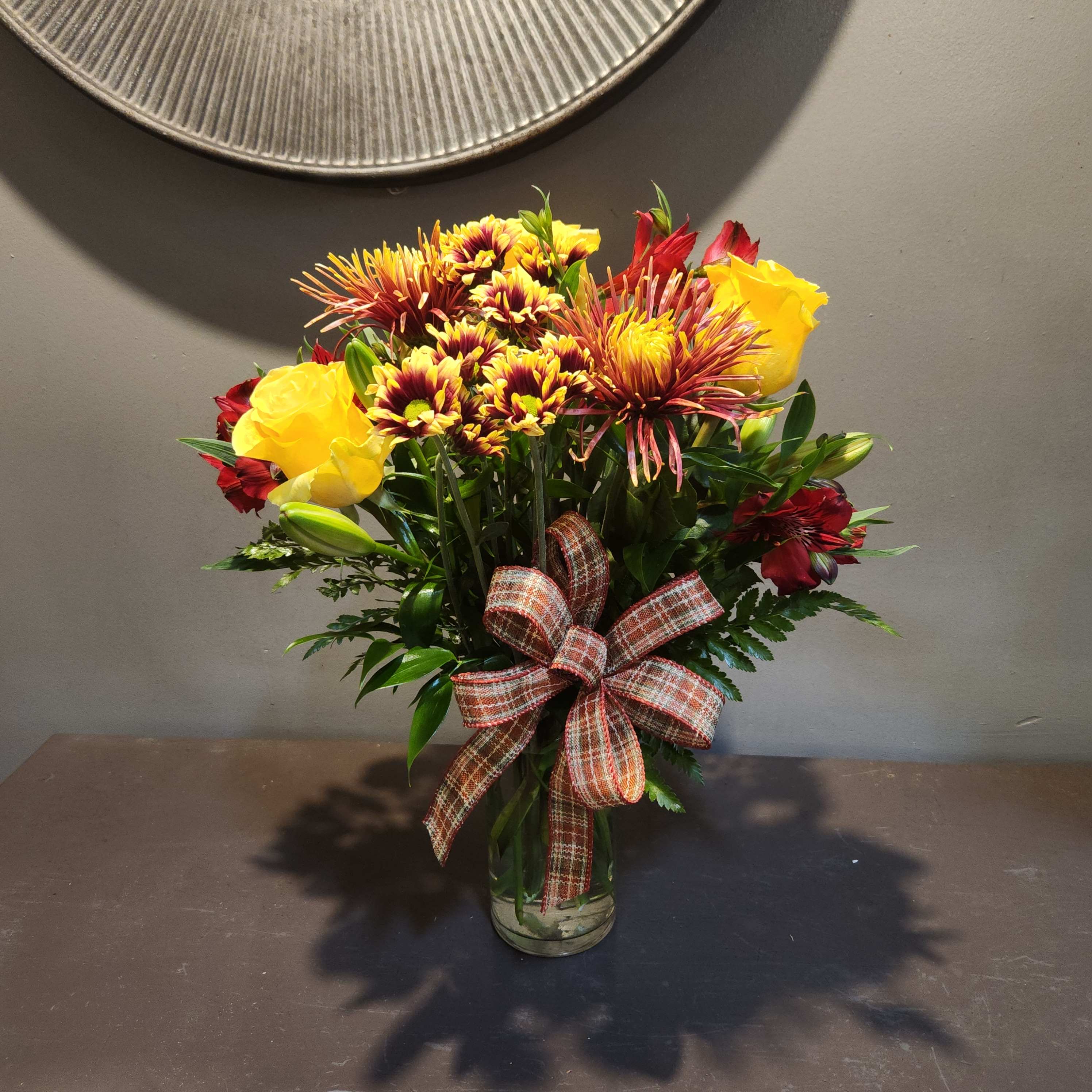 Bouquet of yellow roses and red chrysanthemums in a glass vase with a plaid ribbon