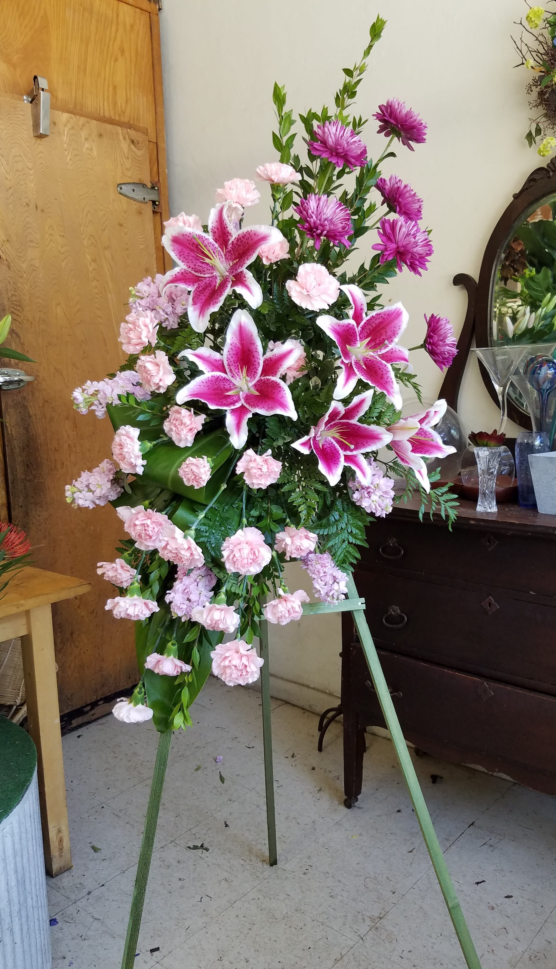 Peaceful Remembrance standing spray - **Please note** All standing sprays require a minimum of 72 hours advance notice. Online orders without this lead time may be subject to cancellation. Thank you for you understanding  A timeless combination of stargazer lilies, pink carnations, pink stock, and lavender mums is arranged on the bias for a modern twist.  This standout sympathy piece makes an excellent floral tribute.