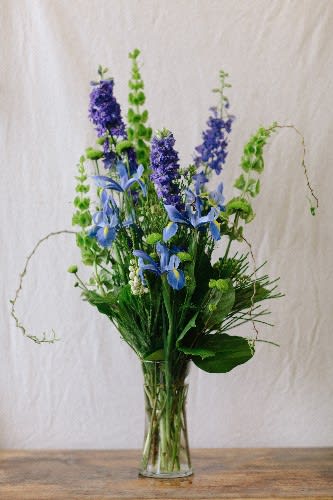 Tall blue and purple floral arrangement in a clear glass vase