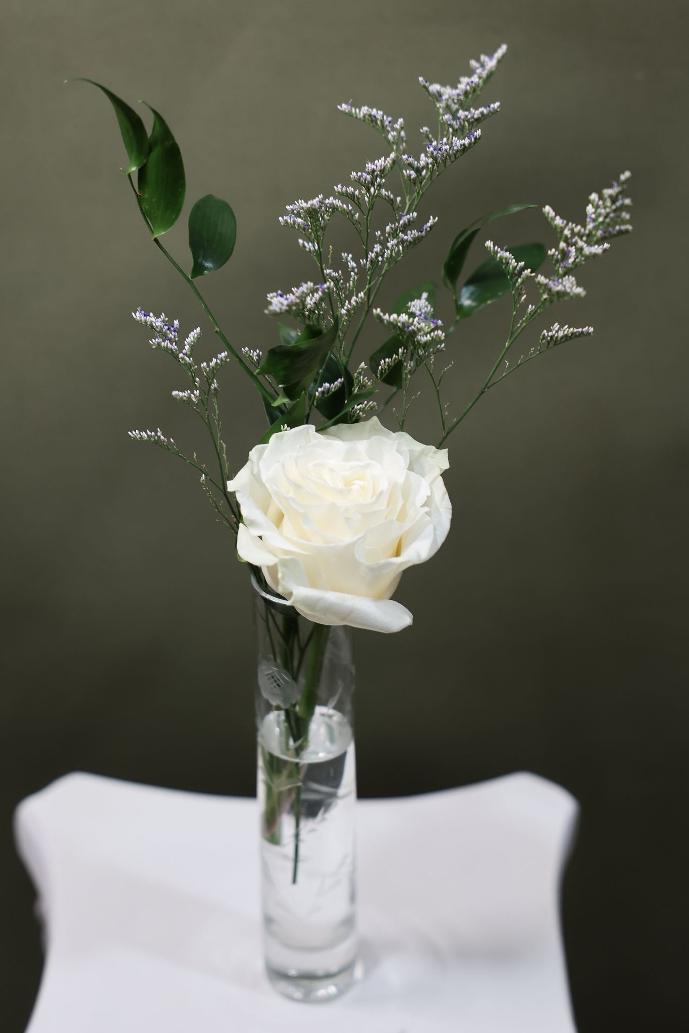 White rose in a clear glass vase with airy purple filler