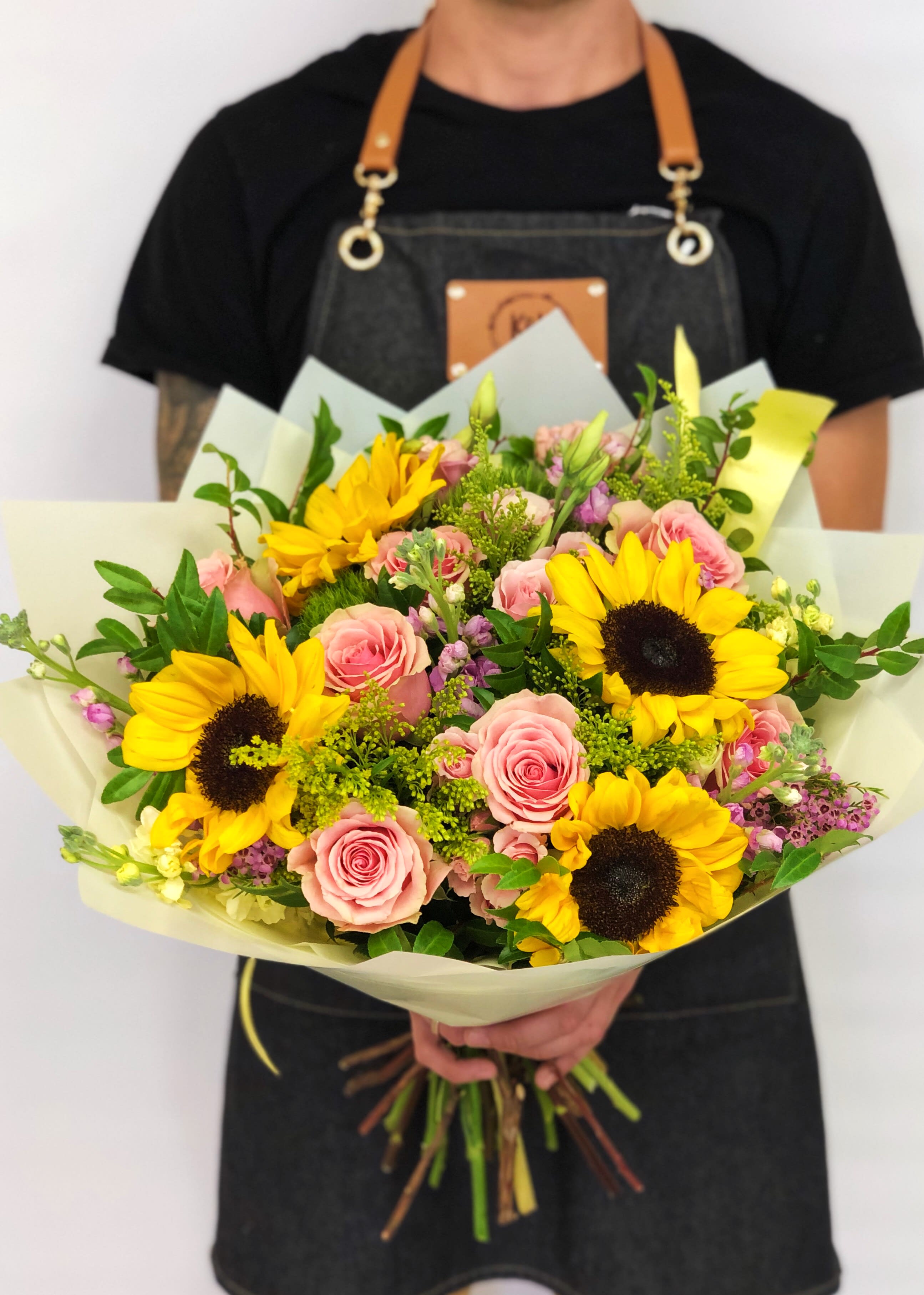 Handheld bouquet of pink roses and yellow sunflowers wrapped in pale paper