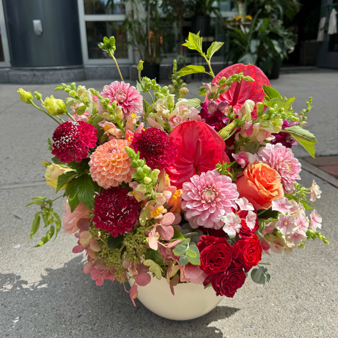 Mixed bouquet in a white bowl vase with pink, red, and peach flowers