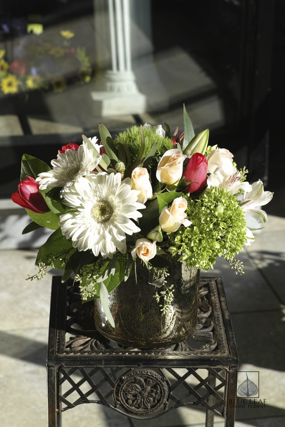 Bouquet of white daisies, pale roses, and red tulips in a glass vase