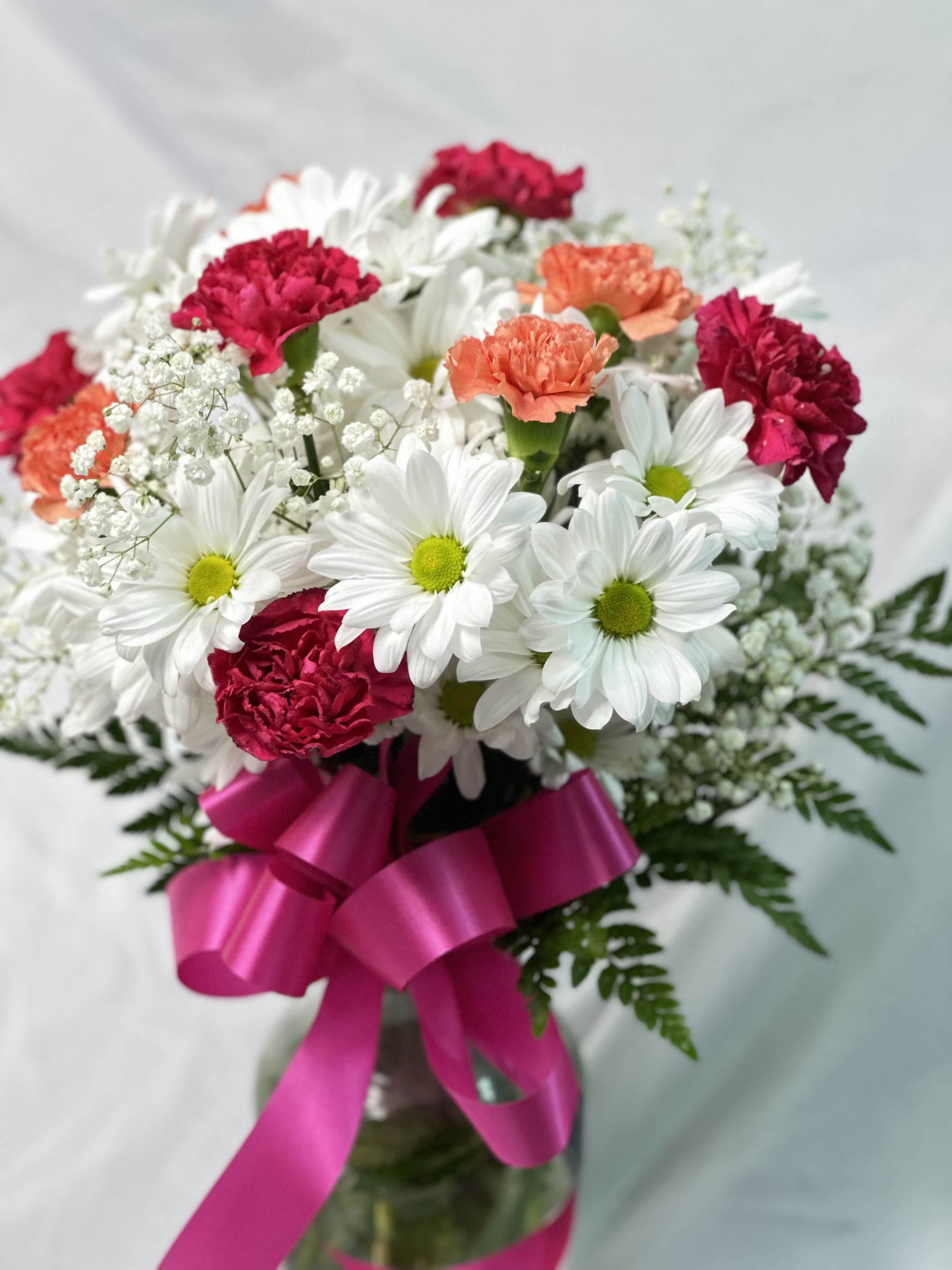 Bouquet of white daisies and pink carnations with a magenta ribbon in a vase