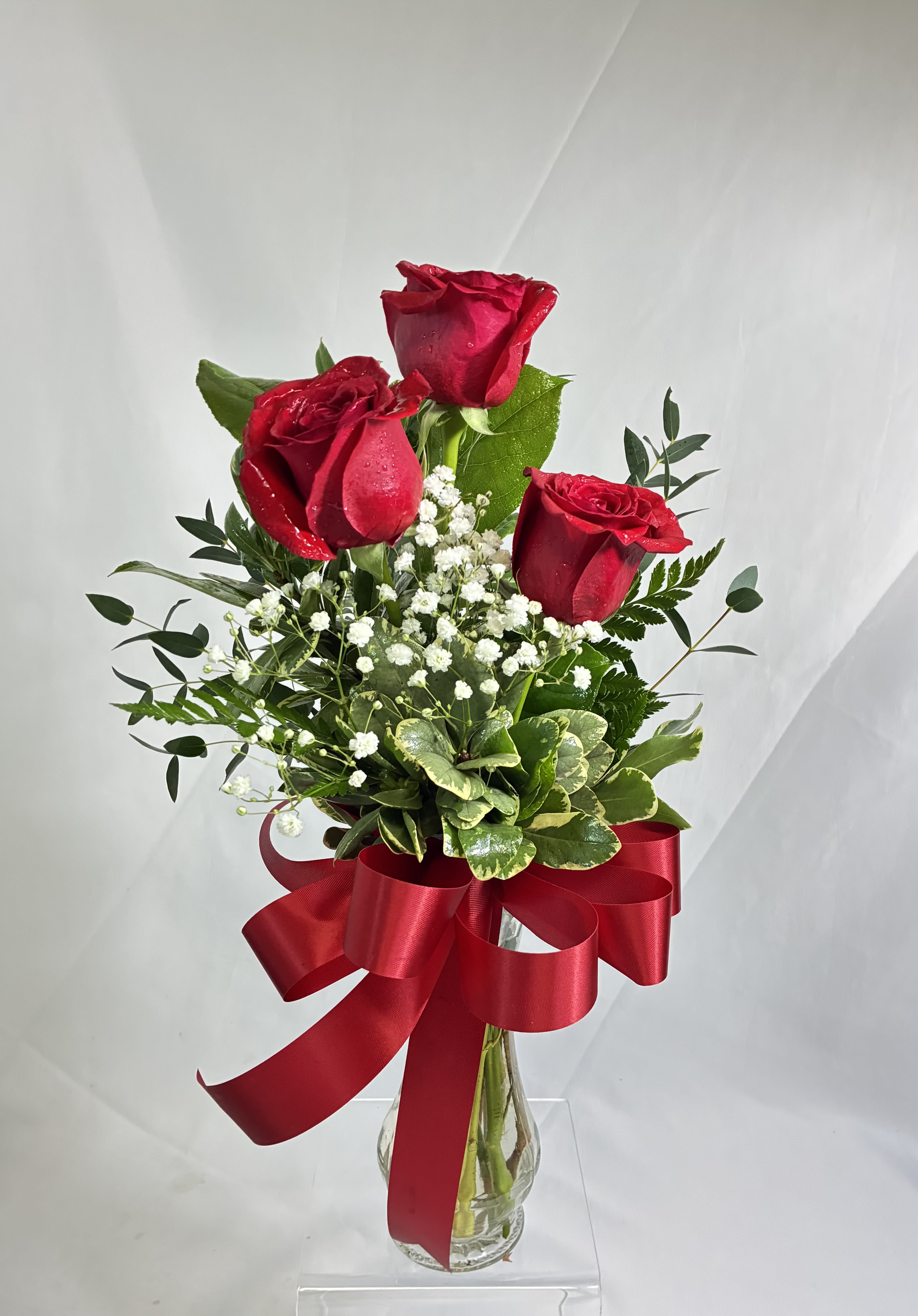 Three red roses in a glass vase with a large red ribbon