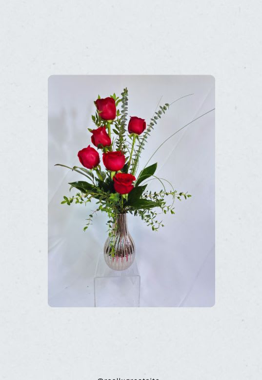 Tall vase arrangement of red roses with airy greenery