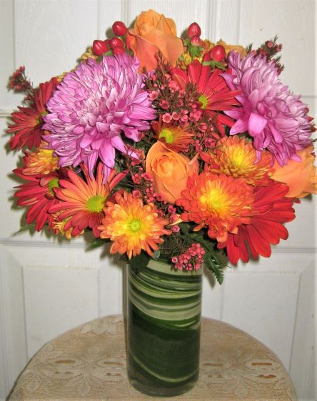 Colorful bouquet of pink, orange, and red flowers in a green glass vase