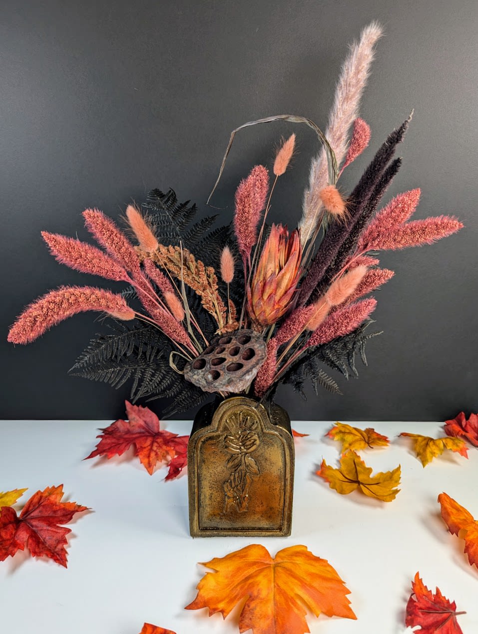 Dried floral arrangement in a decorative vase with autumn leaves