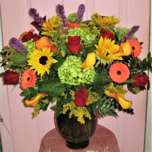 Mixed bouquet of roses, sunflowers, calla lilies, and gerbera daisies in a dark vase