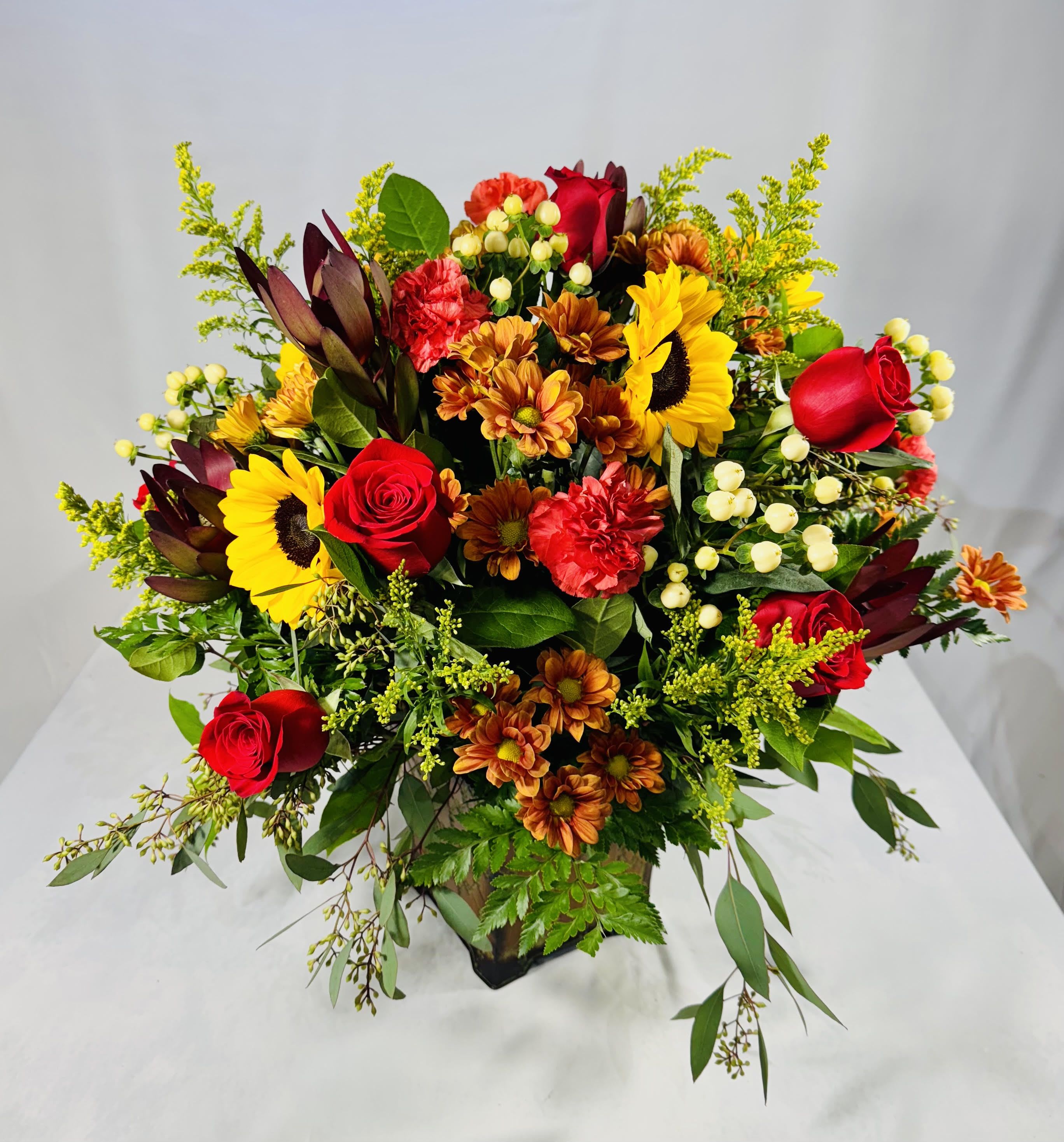 Mixed bouquet with red roses, sunflowers, and orange mums in a vase