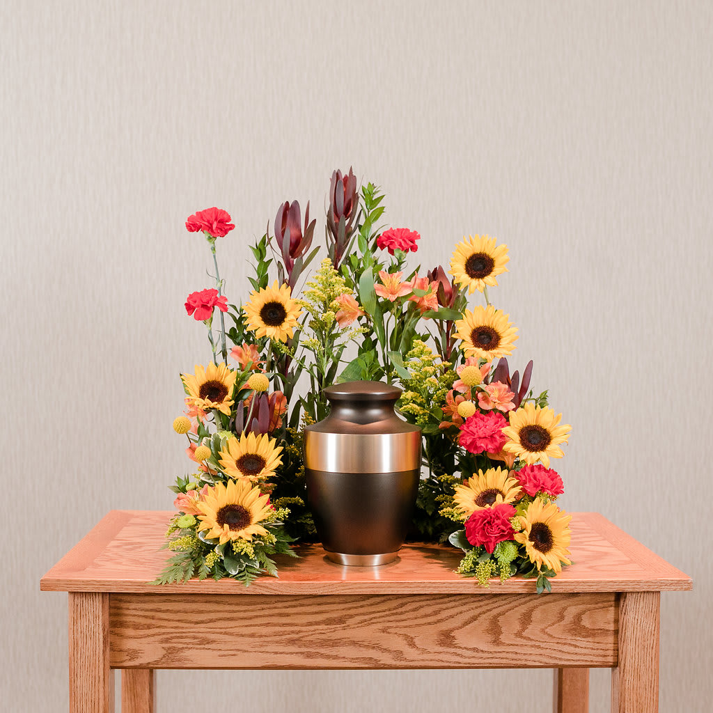 Sunflower and carnation funeral urn arrangement on a wooden table