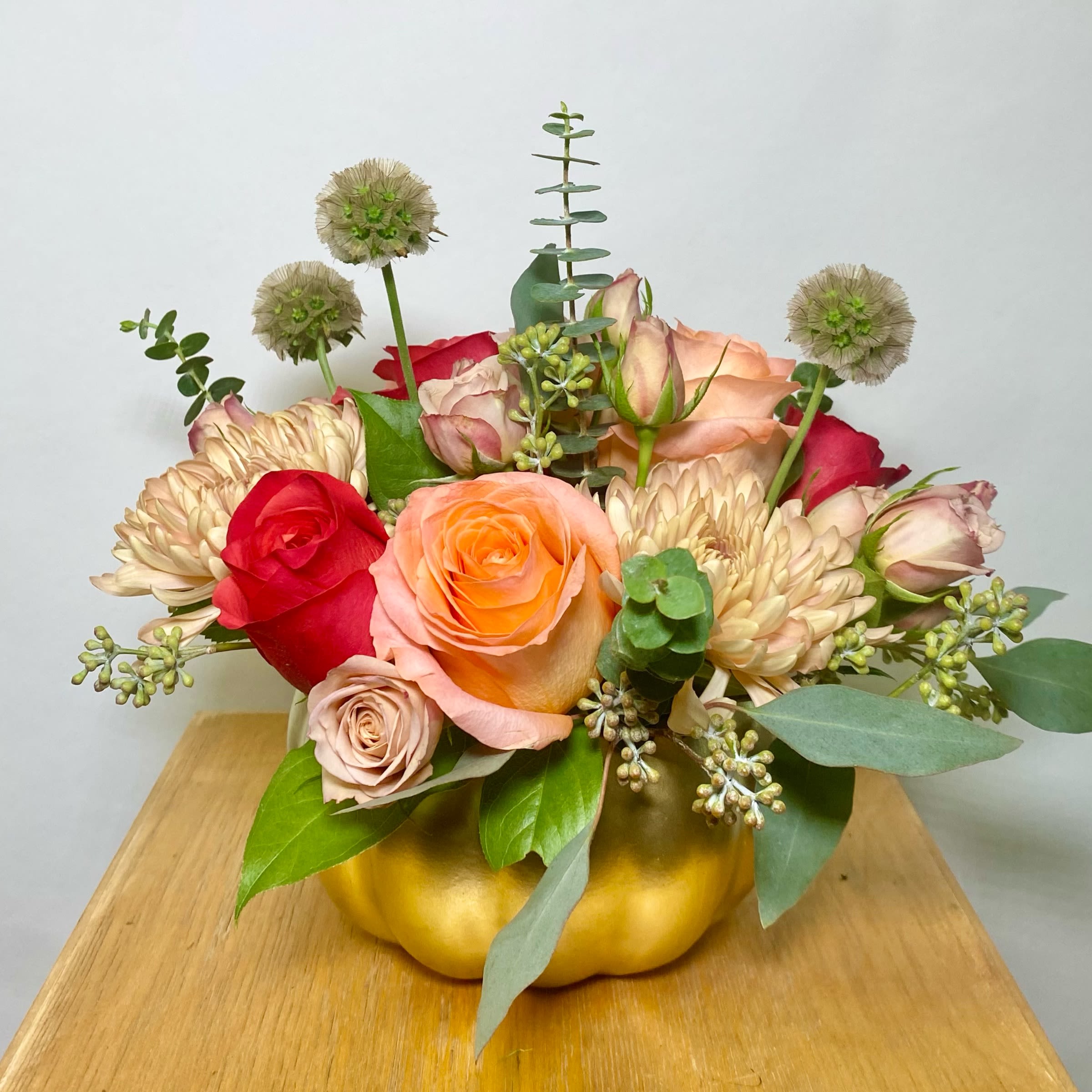 Mixed roses and chrysanthemums arranged in a gold pumpkin container
