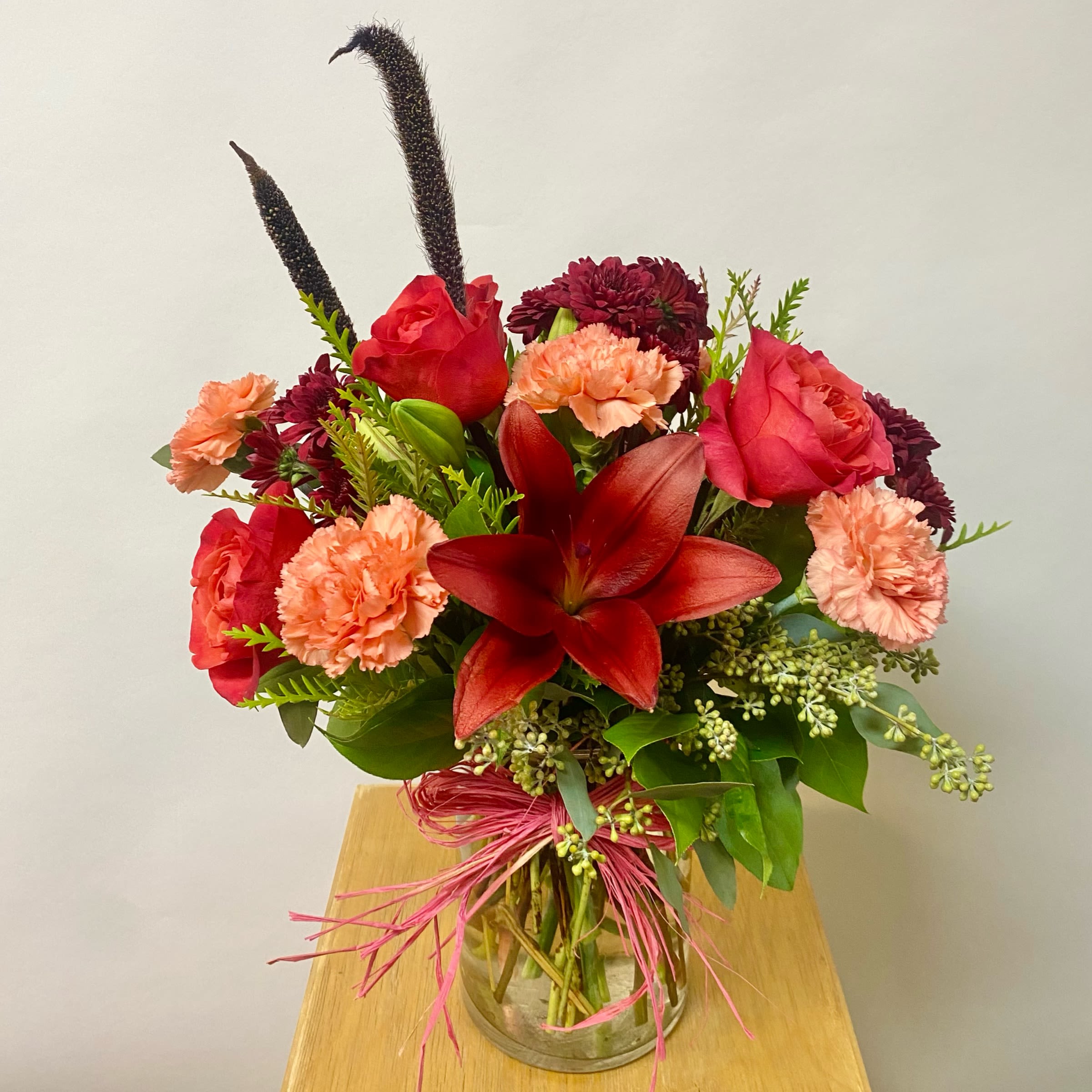 Bouquet of red roses, carnations, and a red lily in a glass vase