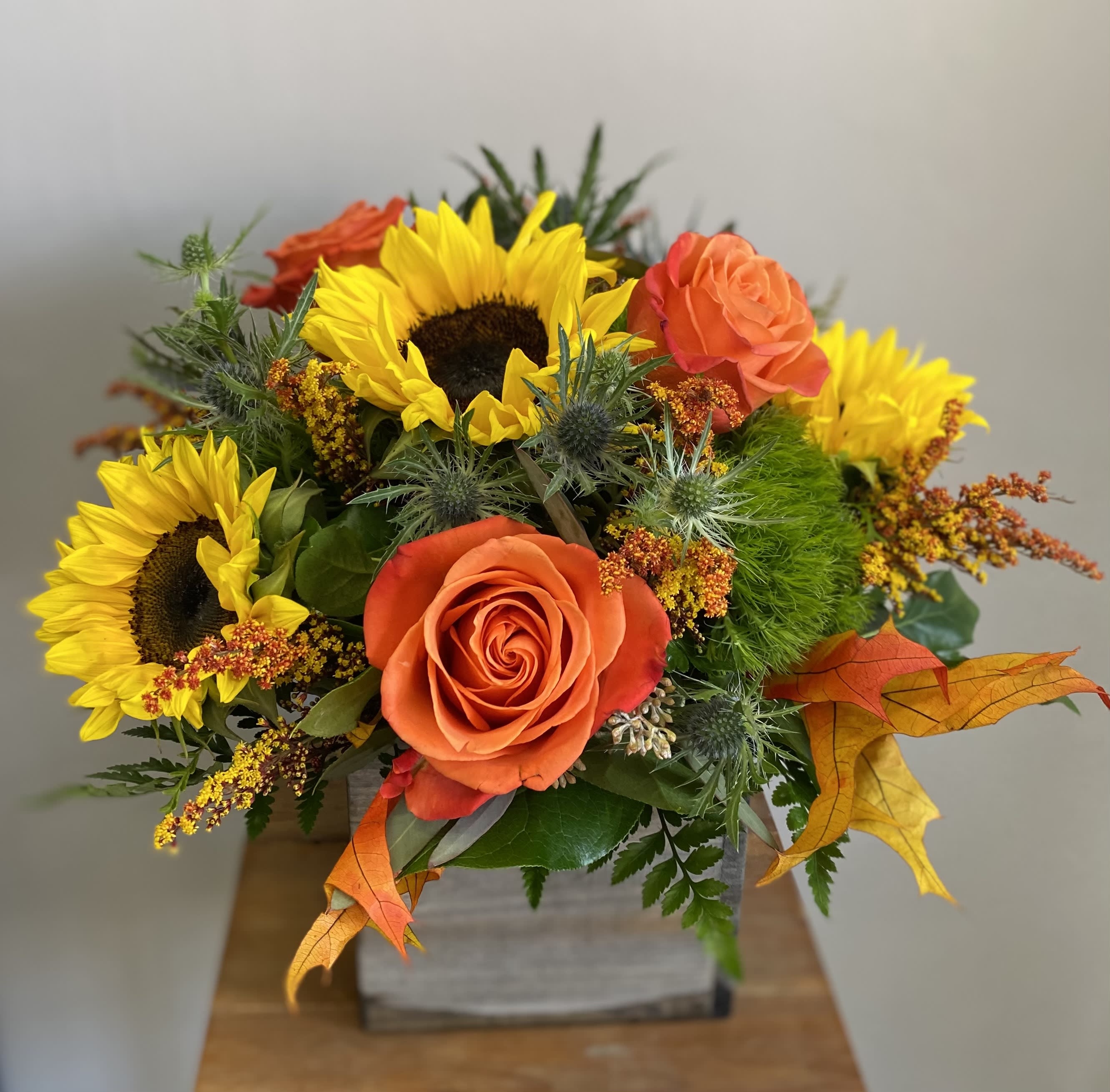 Orange roses and yellow sunflowers in a square container