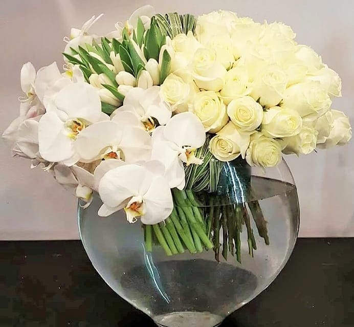 White orchids and pale roses arranged in a clear round vase