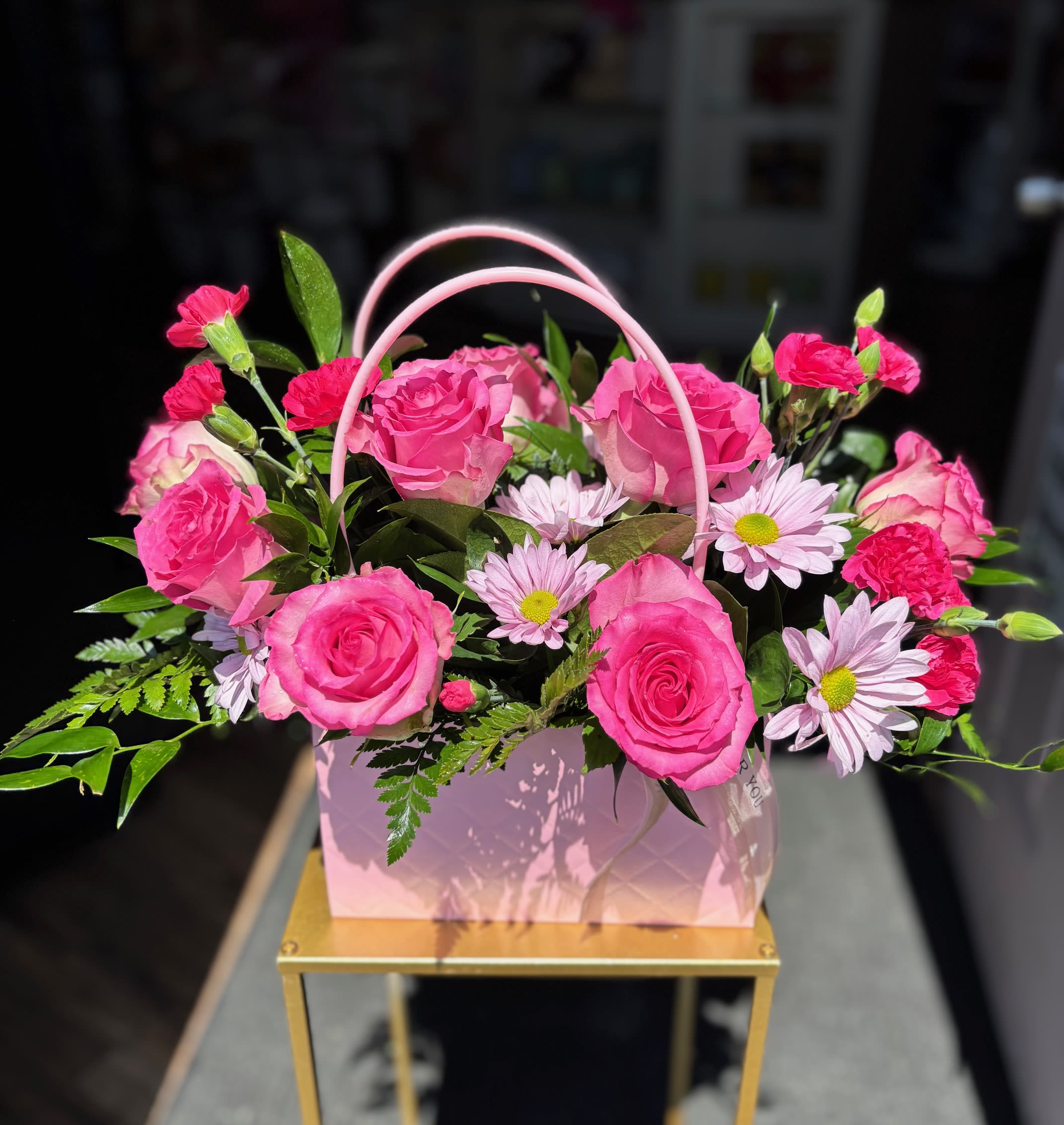 Pink roses and daisies arranged in a pink handled gift box