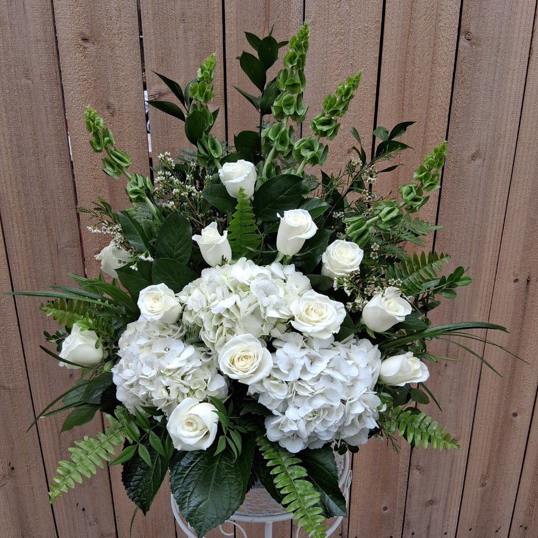 White roses and hydrangeas arranged in a white vase with green foliage.