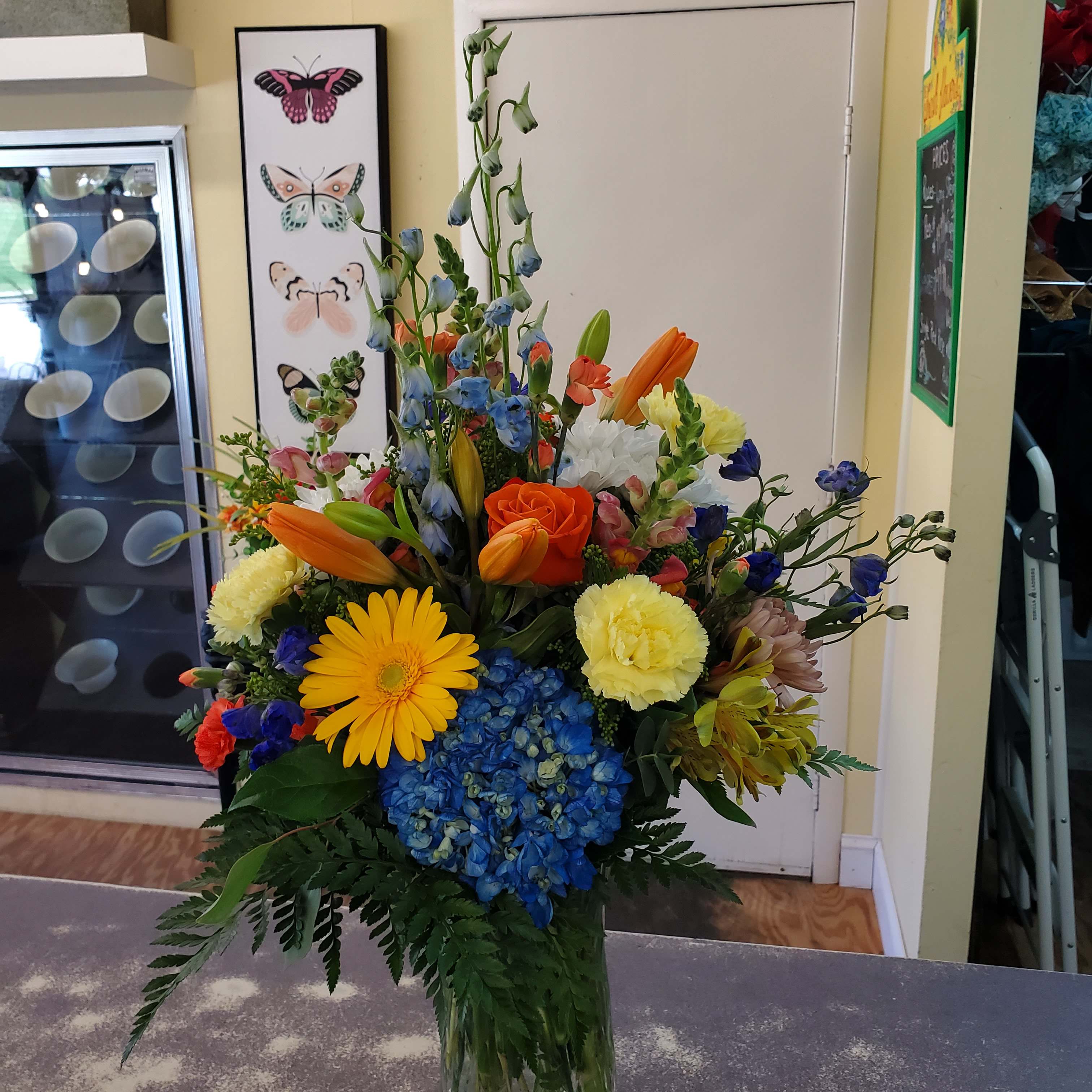 Colorful mixed bouquet in a clear glass vase with roses, lilies, hydrangea, and daisies