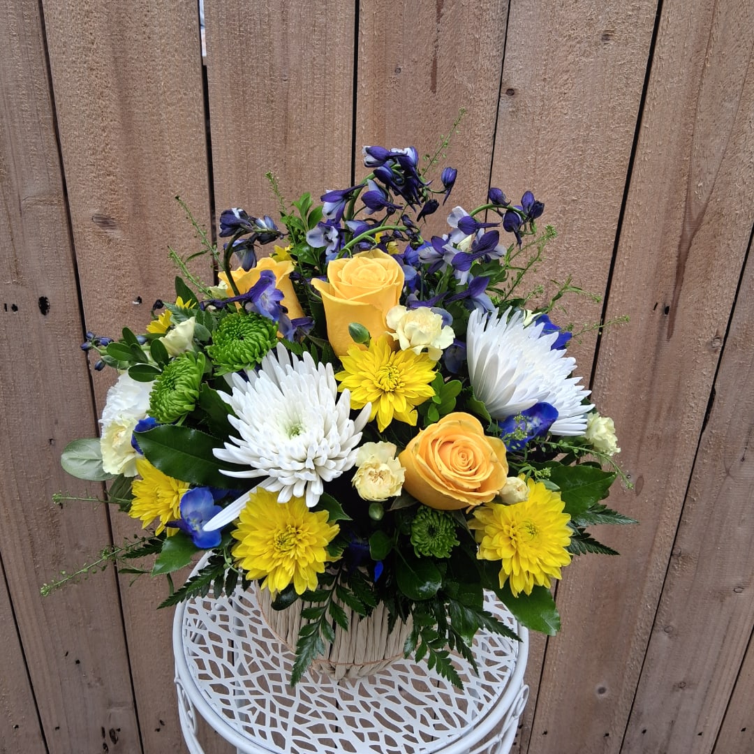 Mixed bouquet with yellow roses, white chrysanthemums, and blue flowers in a basket.