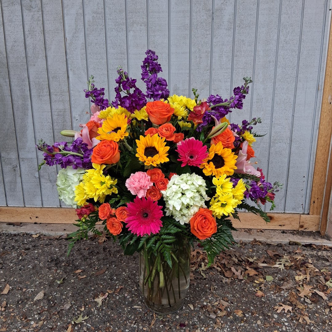 Colorful mixed bouquet in a glass vase with sunflowers, roses, and gerbera daisies