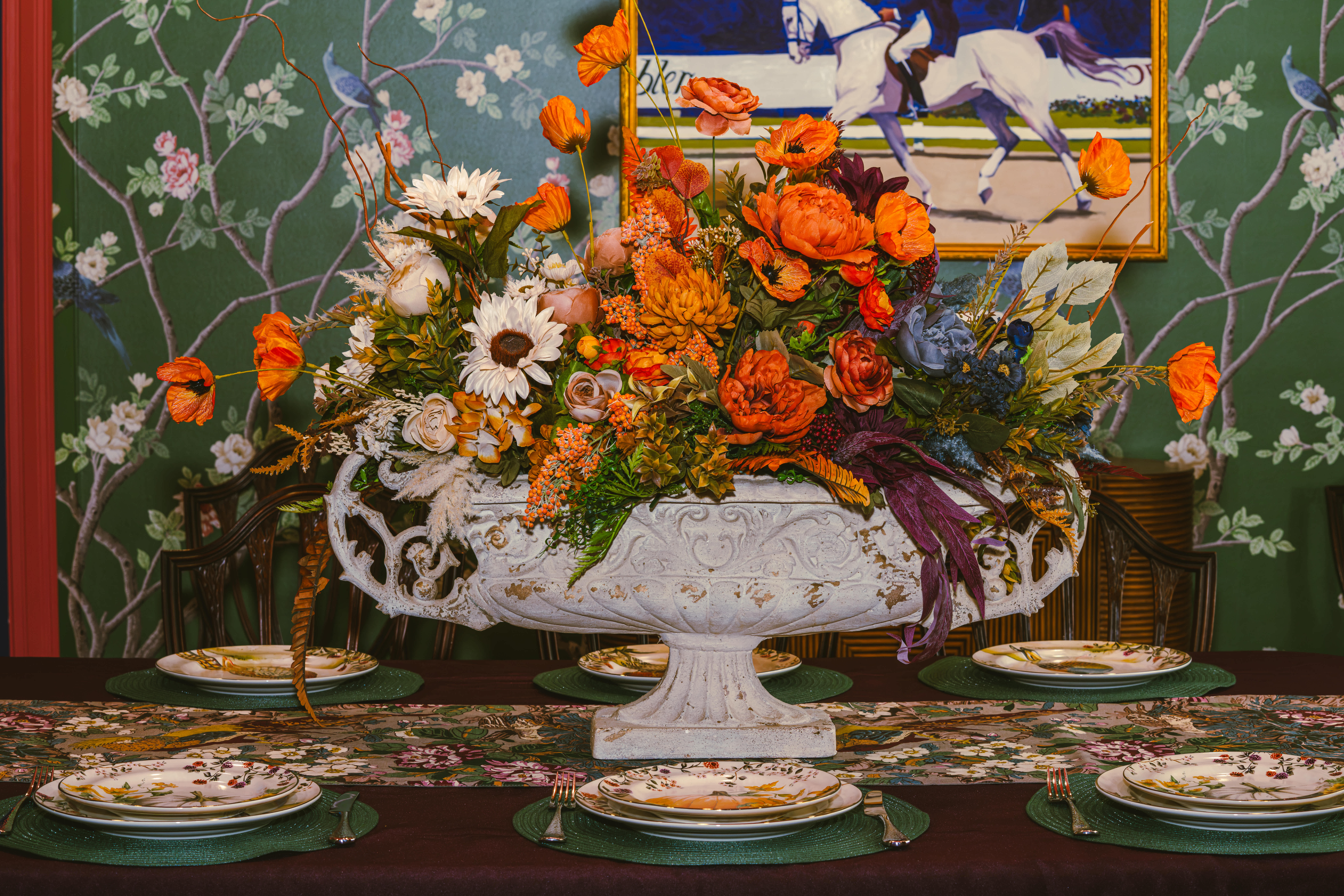 Large orange and white floral centerpiece in an ornate white urn on a dining table