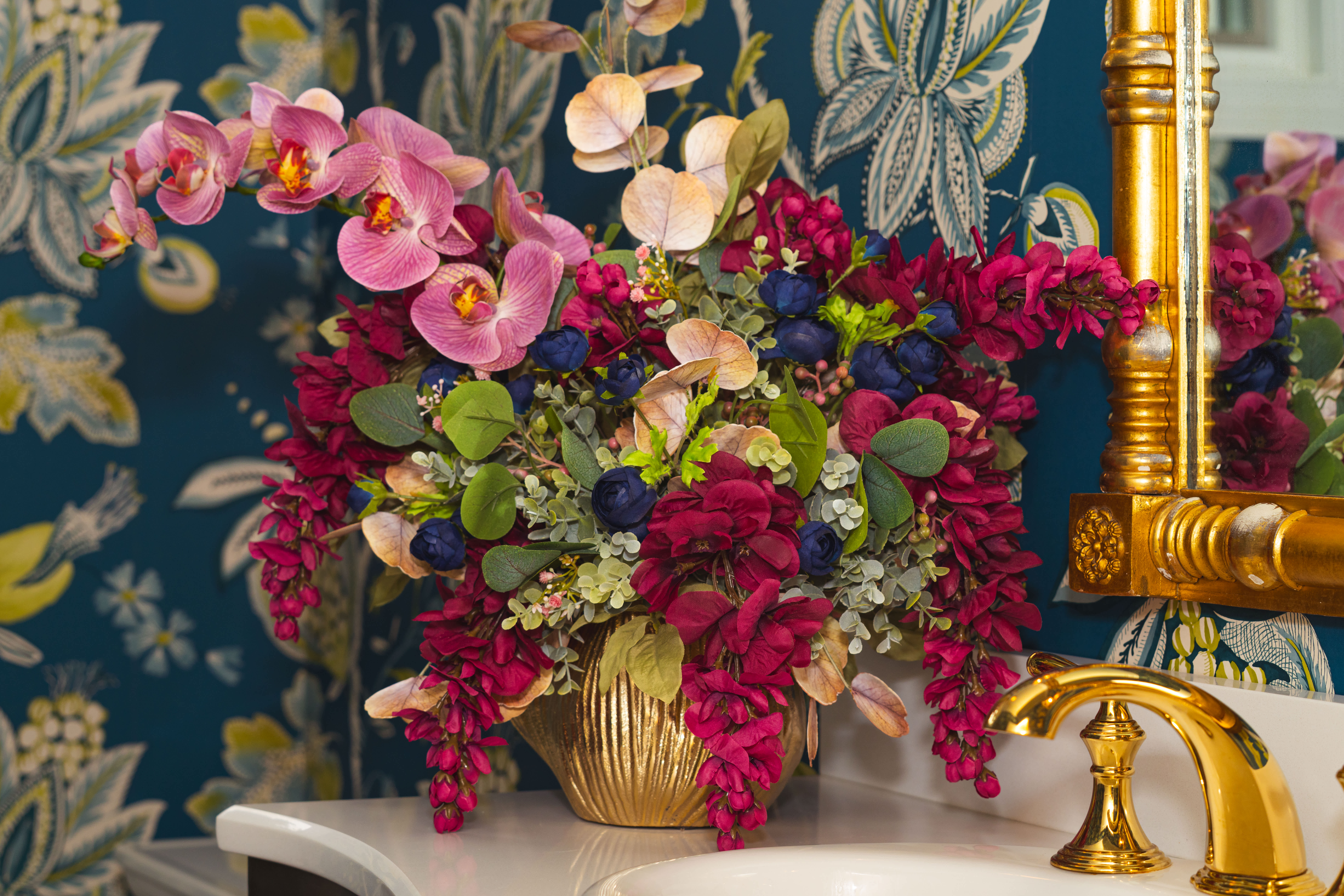 Pink orchids and magenta flowers arranged in a gold vase