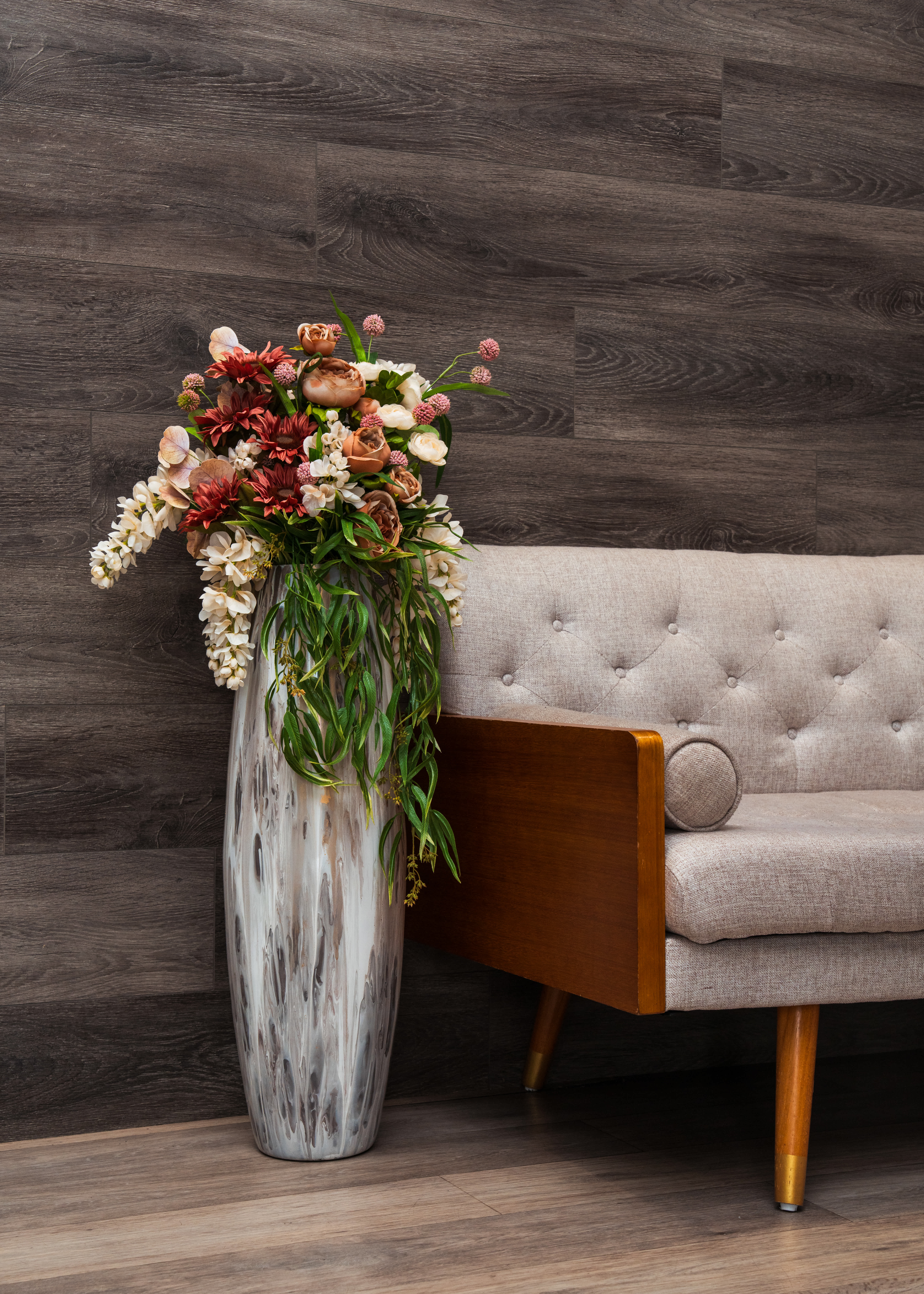 Tall floral arrangement in a silver vase beside a beige sofa
