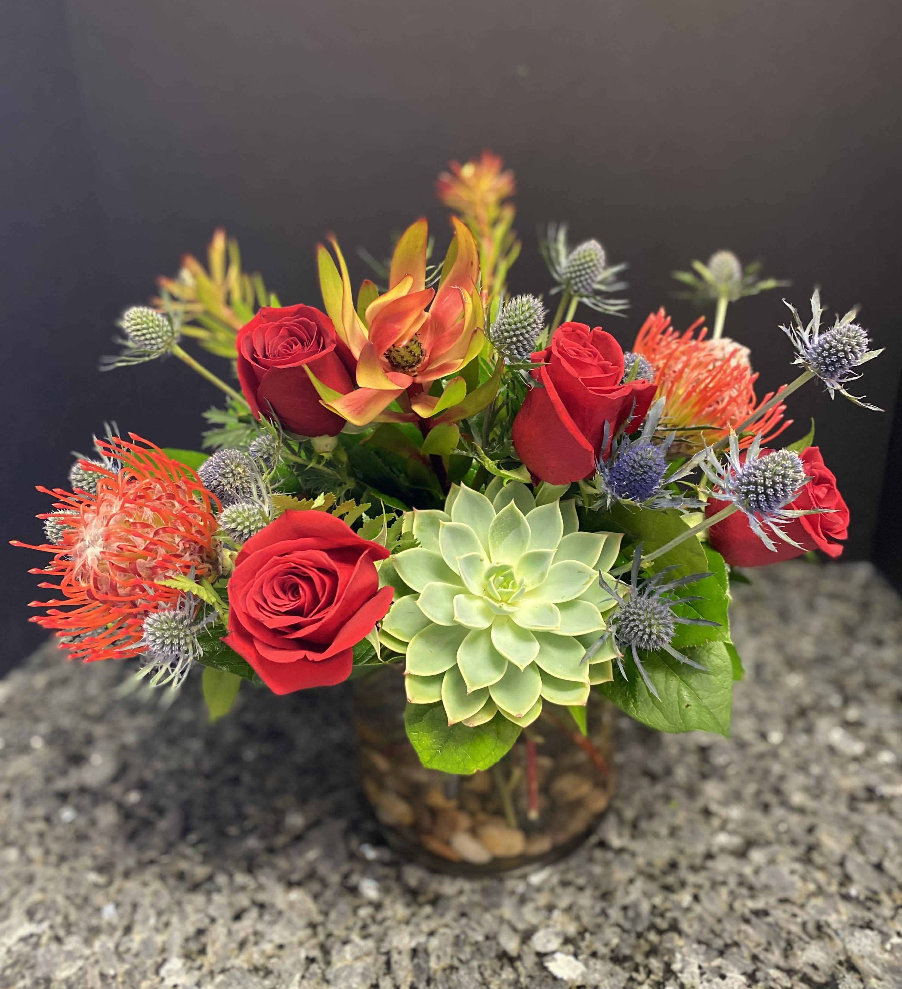 Red roses and a green succulent in a glass vase with spiky accent flowers