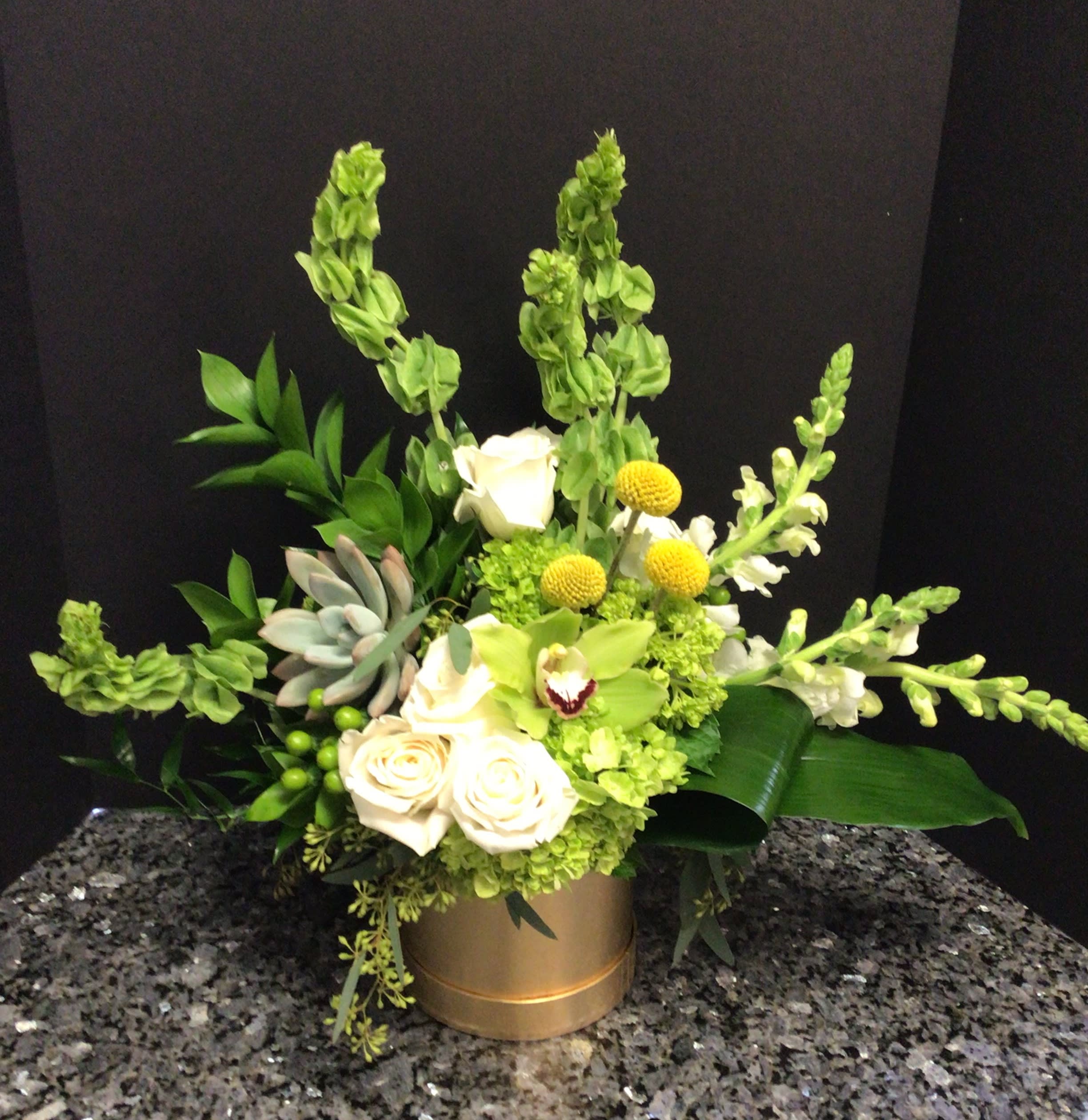 Green and white floral arrangement in a gold container