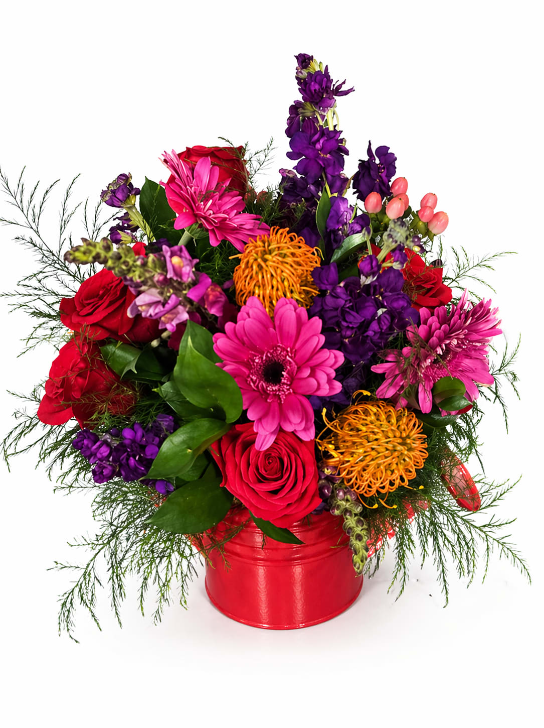 Ruby Radiance Watering Can - A glossy red metal watering can holds a dense, celebratory bouquet that immediately reads as joyful and festive - perfect as a birthday bouquet, a cheerful get-well arrangement, or a bright "thinking of you" gift. The upright, full design gives the person you're sending it to a lively splash of color that feels both tropical and homey, so she'll feel genuinely celebrated the moment it's set on a table.  This mixed arrangement combines red roses with hot pink gerbera daisies, purple snapdragons, orange spider-like blooms and other seasonal accents, all set against deep green foliage for contrast and texture. The composition is compact and upright, with a glossy red metal container (watering can) that doubles as a keepsake hard good. Container included.