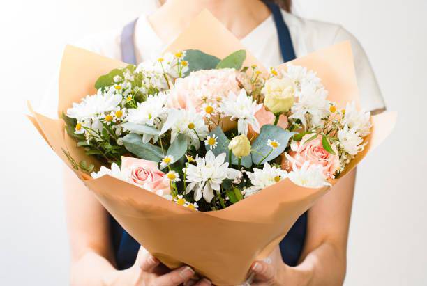 Bouquet of white daisies and pale pink roses wrapped in tan paper