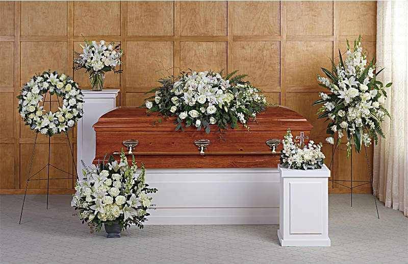 White funeral casket surrounded by white floral sprays and wreaths